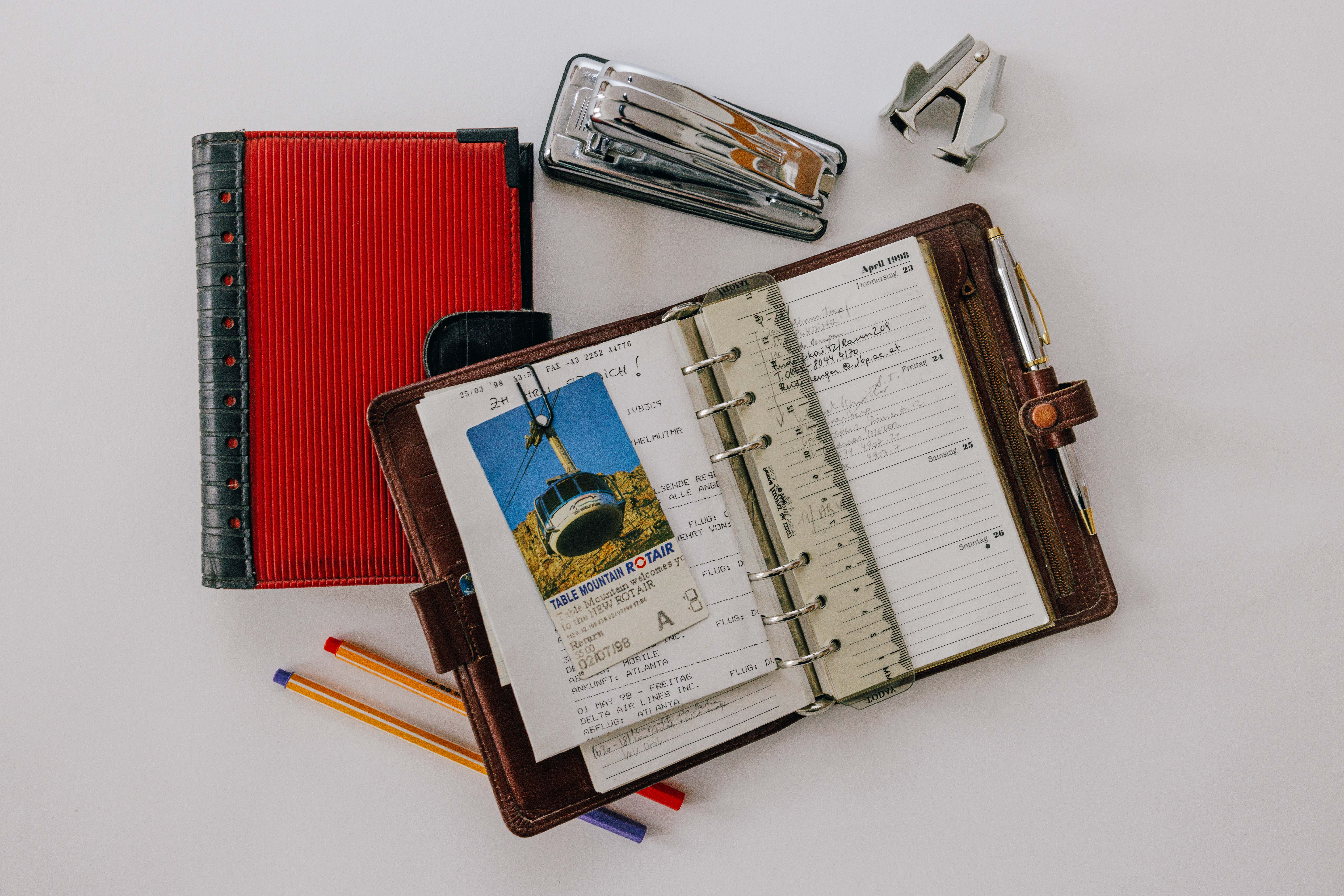 Das Bild zeigt einen offenen und einen geschlossenen Filofax, einen Hefter, einen Klammernentferner und mehrere Stifte.