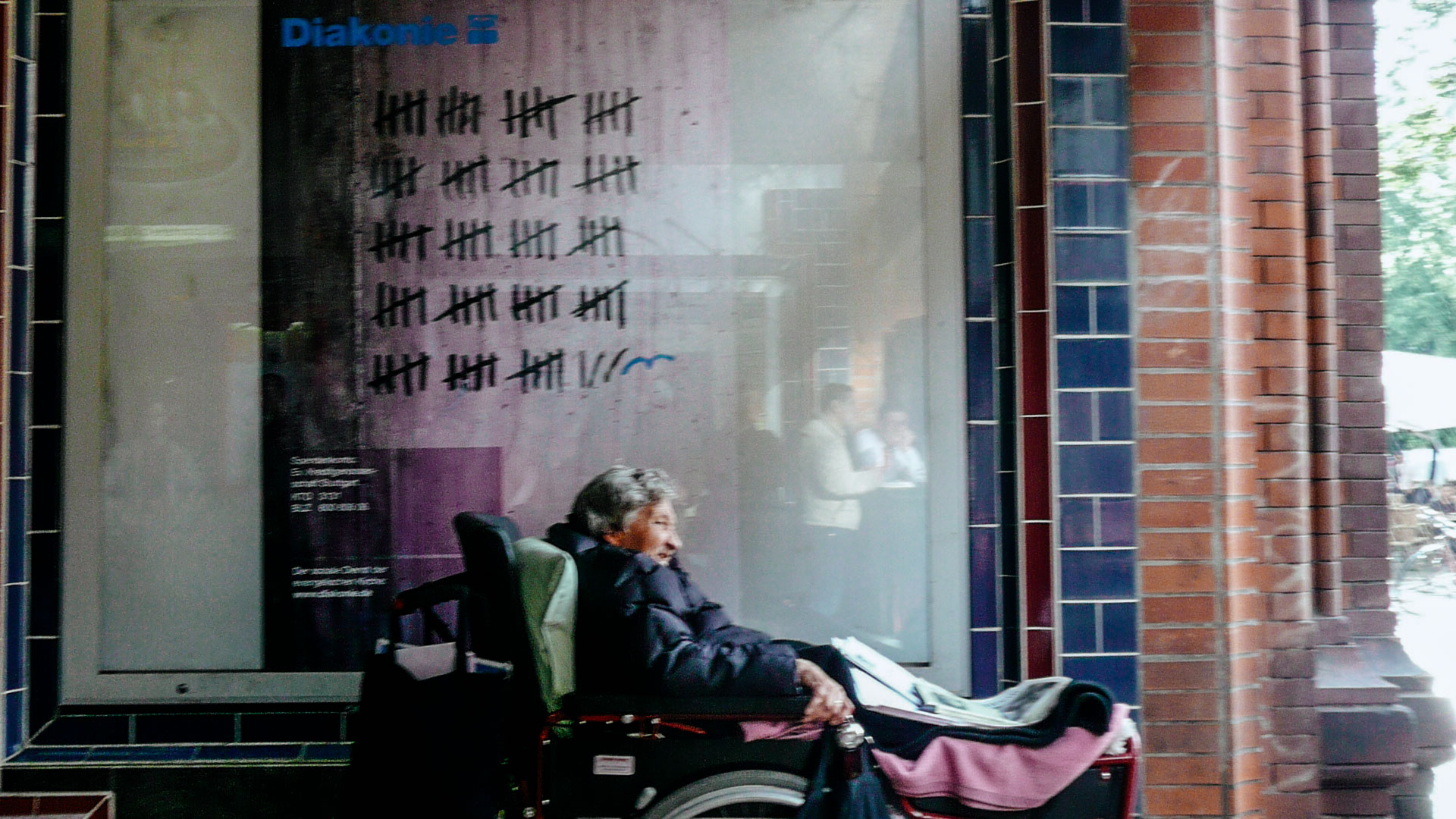 Eine Frau im Rollstuhl, in einer U-Bahn-Passage, vor einem Plakat der Diakonie.